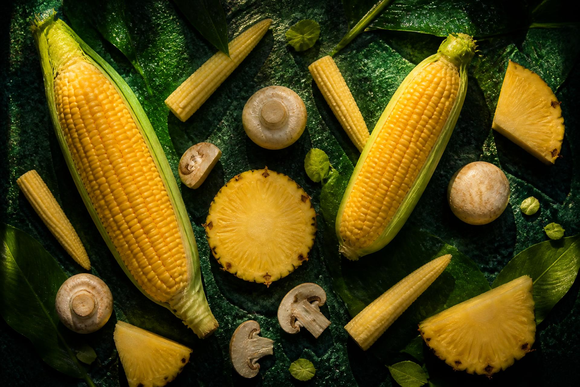 Fresh sweet corn, baby corn, mushrooms and pineapple on a dark green surface